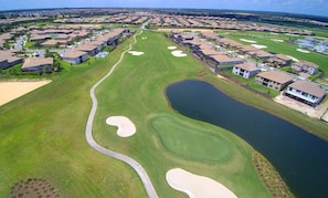 An aerial view of a golf course with sand bunkers, a pond, and residential buildings. - 4BR Home With Private Pool & Disney Themes (Davenport)