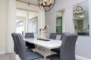 A modern dining area with a white table, grey chairs, and a decorative horse sculpture. - 4BR Home With Private Pool & Disney Themes (Davenport)