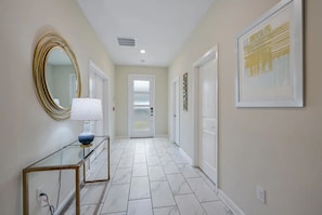 A hallway with a glass console table, a gold-framed mirror, and a framed artwork on the wall. - Luxury 9BR Villa w/ Private Pool & Themes (Kissimmee)