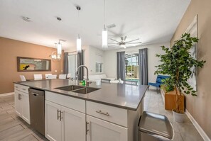 A modern kitchen with a central island, a dining area with a blue chair, and a ceiling fan. - Stylish 4BR Townhome w/ Pool Near Disney (Kissimmee)
