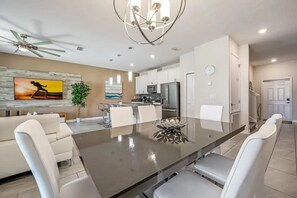 A modern kitchen with white cabinets, stainless steel appliances, and a dining area with a large table and white chairs. - Stylish 4BR Townhome w/ Pool Near Disney (Kissimmee)