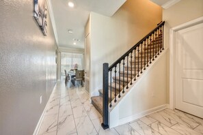 A hallway with a marble floor leading to a staircase with a black balustrade. - Orlando Escape: 4BR w/ Private Pool (Davenport)