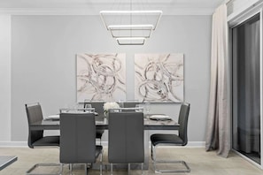 A dining area with a rectangular table, four chairs, and two abstract paintings on the wall. - Family Villa Private Pool + Fun Themes (Davenport)