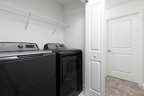 A laundry room with two front-loading washers and dryers, a white door, and a ceiling-mounted drying rack. - Storey Lake 4BR Townhome w/ Private Pool (Kissimmee)