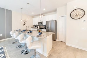A modern kitchen with white cabinets, stainless steel appliances, and a central island with bar stools. - Home w/ Private Pool 10 min to Disney (Kissimmee)