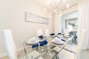 A dining area with a glass table, white chairs, and a chandelier. - Home w/ Private Pool 10 min to Disney (Kissimmee)