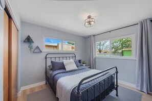 Bedroom with a dark metal bed, soft blue bedding, and two windows. - Modern Farmhouse in Uptown ABQ (Albuquerque)