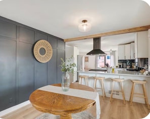 A modern kitchen with a central island, wooden stools, and a dining table with a vase. - Modern Farmhouse in Uptown ABQ (Albuquerque)