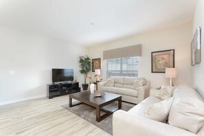 A living room with a sofa, a coffee table, a TV, and a plant. - Spacious Townhome w/ Pool Storey Lake (Kissimmee)