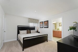 A bedroom with a bed, a nightstand, a desk, and a view into the kitchen. - Spacious Townhome w/ Pool Storey Lake (Kissimmee)