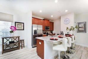 A modern kitchen with wooden cabinets, stainless steel appliances, and a central island with bar stools. - Spacious Townhome w/ Pool Storey Lake (Kissimmee)