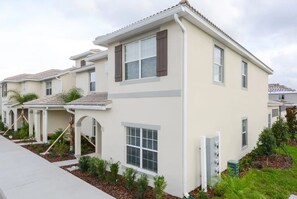 A row of modern, two-story townhouses with a flat roof, large windows, and a small front porch. - Spacious Townhome w/ Pool Storey Lake (Kissimmee)
