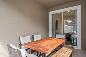 A dining area with a wooden table and chairs, a glass door leading to an interior space, and a hanging light fixture. - Home w/ Private Pool & Disney/marvel Themes (Davenport)