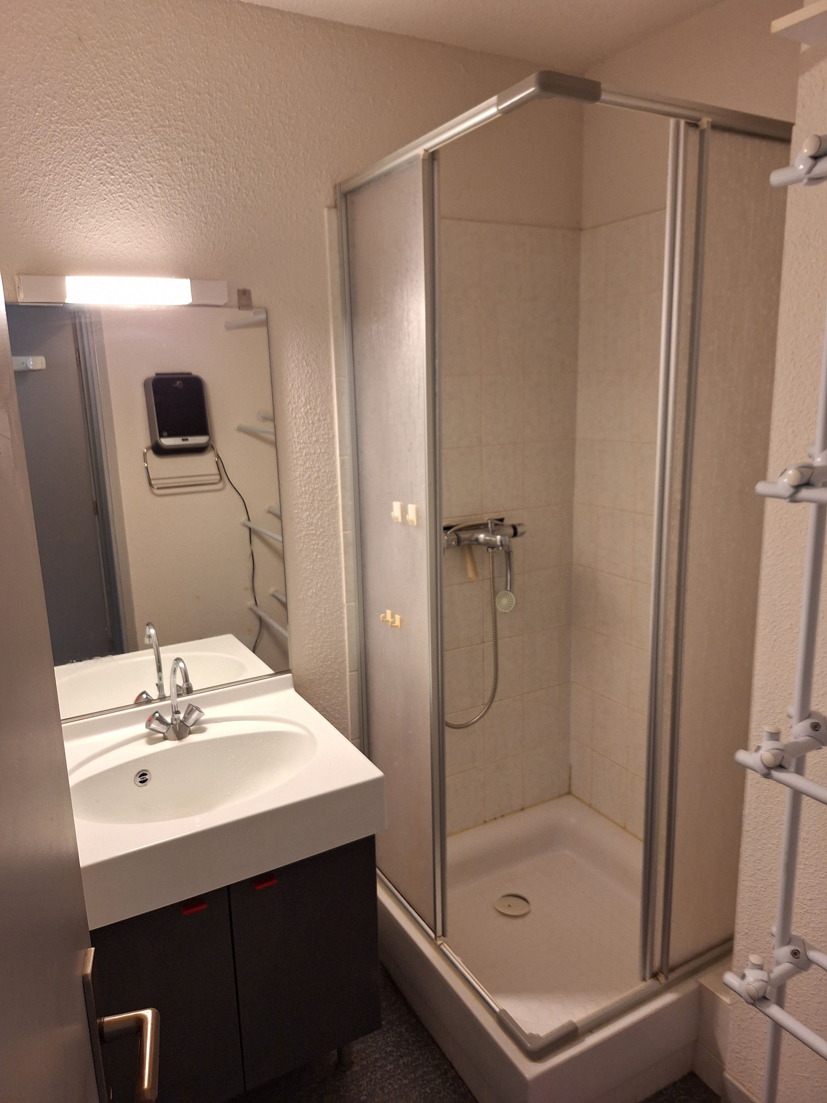 Une salle de bain avec un lavabo blanc, un miroir, une douche à parois de verre et un porte-serviettes.