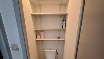 Une petite salle de bain étroite, avec des toilettes, des étagères et une boîte fixée au mur.