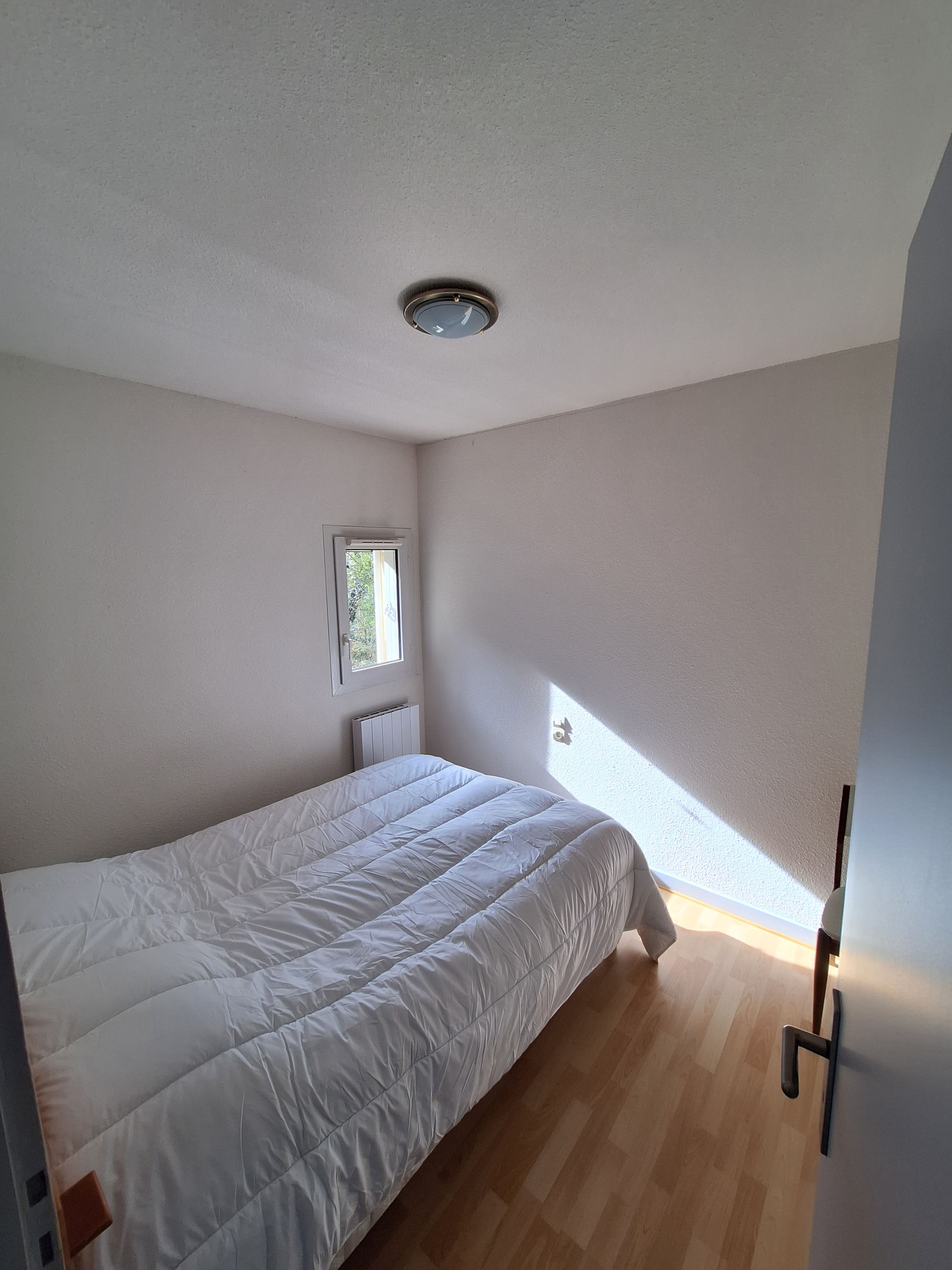 Une chambre à coucher avec un lit, une fenêtre, un radiateur et une porte.