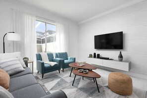 A modern living room with a sofa, armchair, coffee table, ottoman, and a TV mounted on the wall. - Home w/ Private Pool & Mickey/star Wars Themes (Davenport)