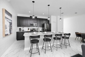 A modern kitchen with dark cabinets, a central island with bar stools, and pendant lighting. - Home w/ Private Pool & Mickey/star Wars Themes (Davenport)