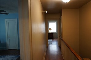 A hallway with a wooden floor, a white door, and a lamp near a window. - Delightful 2 bedroom townhouse in Hamlet (Hamlet)
