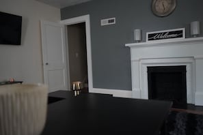 A room with a dark wooden table, a white door, a fireplace with a 'Welcome' sign, and a clock on the wall. - Delightful 2 bedroom townhouse in Hamlet (Hamlet)