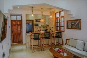 A compact living space with a kitchenette, a dining area with wooden chairs, a sofa, and a coffee table. - Luxury Heritage 2 bedroom apartment with courtyard / Nyumbani Stonetown (Zanzibar)