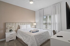 Une chambre d’hôtel avec un lit, une table de chevet avec une lampe, un bureau avec une télécommande et une fenêtre avec des stores.