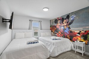 A hotel room with two beds, a large mural of Mickey and Minnie Mouse, a TV mounted on the wall, and a small table with a lamp. - Resort Escape 10 Min From Disney Storey Lake (Kissimmee)