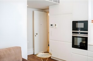 Moderni keittiö, jossa on integroidut kodinkoneet, lasitasoinen pöytä ja ovi, joka johtaa toiseen huoneeseen.