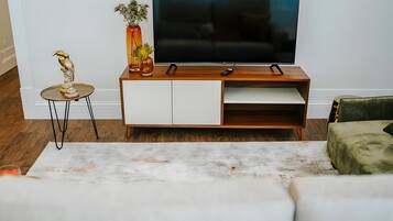 Een moderne woonkamer met een houten tv-meubel, een flatscreen televisie, een klein tafeltje met een sculptuur en een groene fauteuil.