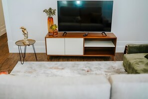 Een moderne woonkamer met een houten tv-meubel, een flatscreen televisie, een klein tafeltje met een sculptuur en een groene fauteuil.
