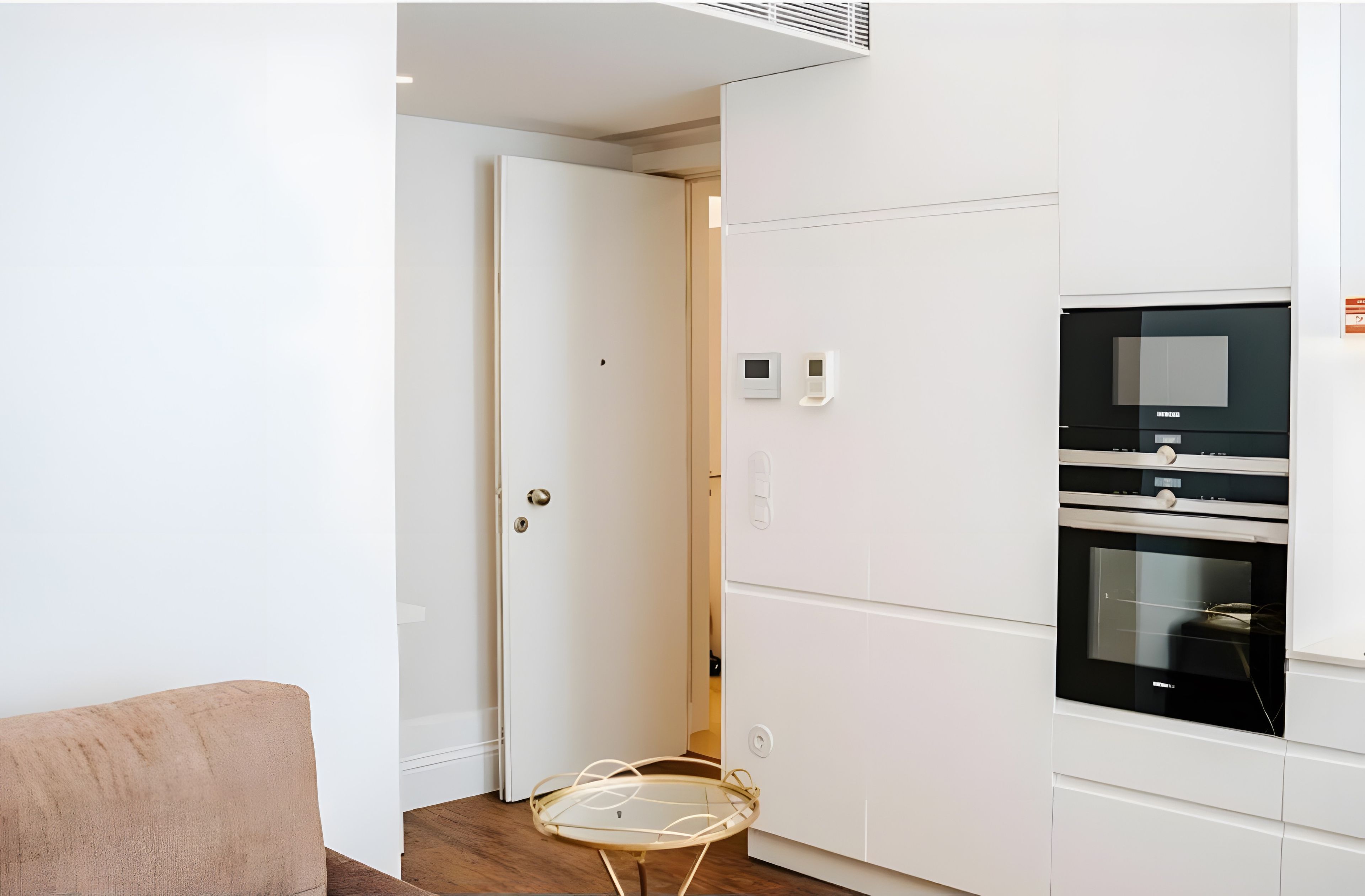 Een moderne keuken met inbouwapparatuur, een glazen tafel en een deur die naar een andere kamer leidt.