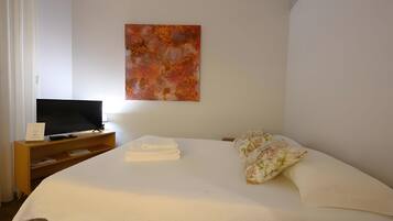 Een hotelkamer met een bed, een televisie op een houten standaard, een schilderij aan de muur en een bloemenkussen.