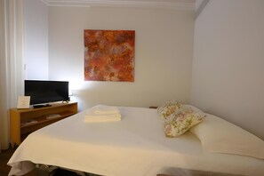 Een hotelkamer met een bed, een televisie op een houten standaard, een schilderij aan de muur en een bloemenkussen.