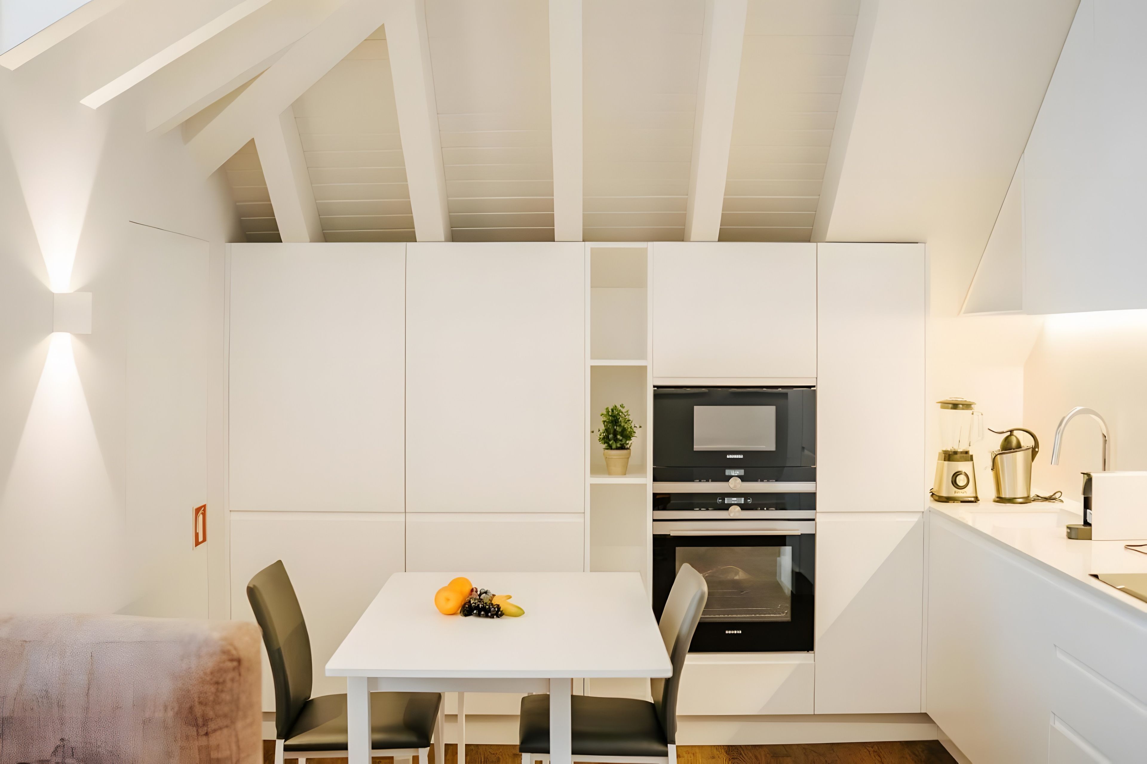 Una cocina moderna con armarios blancos, horno empotrado y una zona de comedor con mesa y sillas.