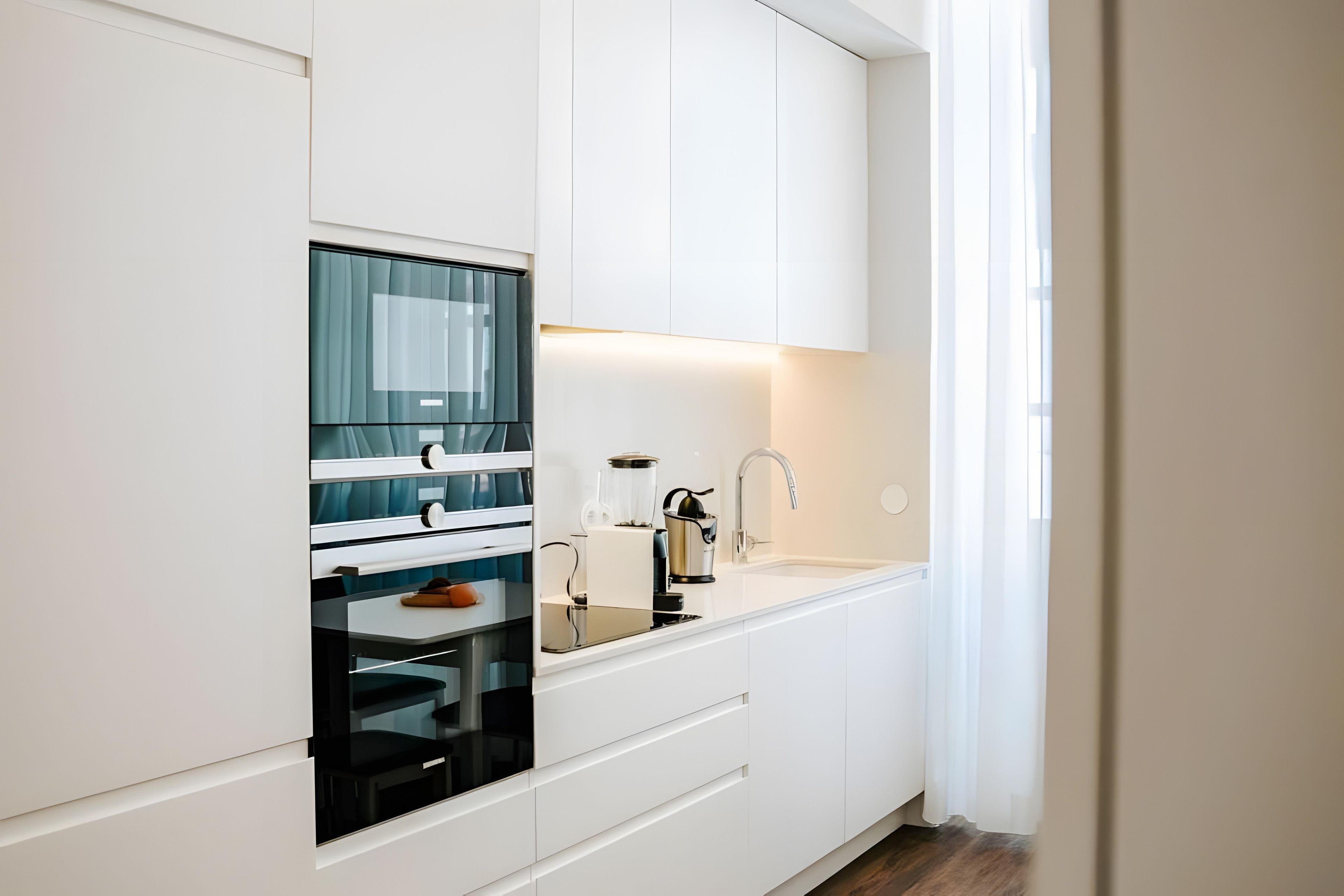 Una cocina moderna con armarios blancos, horno empotrado y pileta de acero inoxidable.