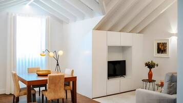 A modern living room with a dining area, featuring a TV, artwork, and a vase with flowers.