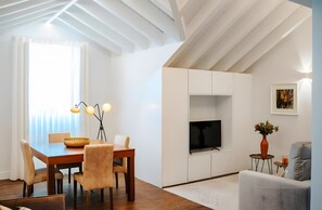 A modern living room with a dining area, a flat-screen TV, and a painting on the wall. - Apartment 'Guerreiro - T1 3A' (Viana do Castelo)