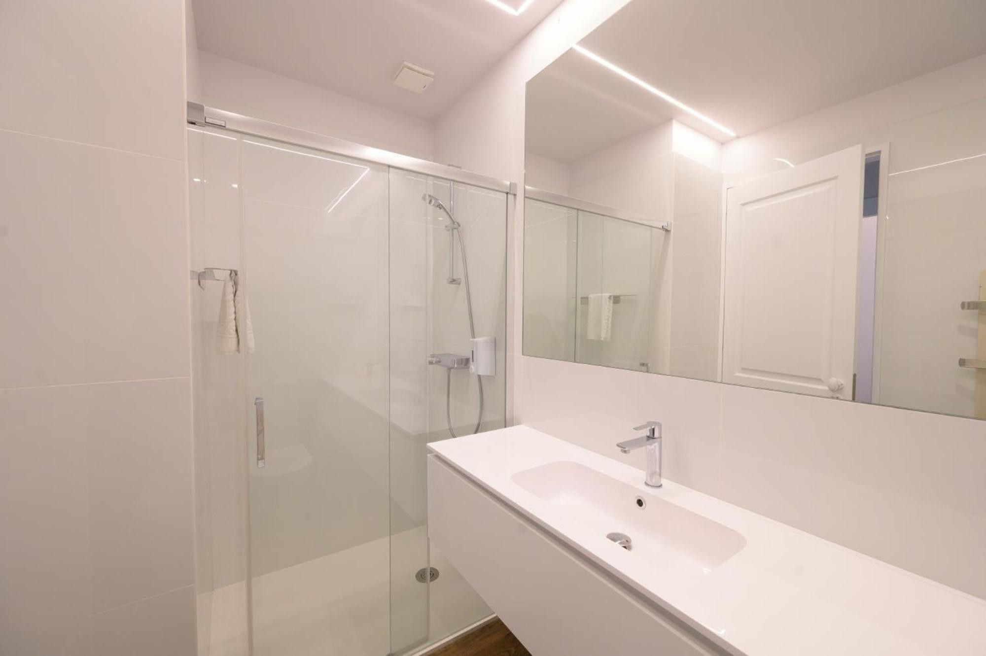 A modern bathroom with a glass shower enclosure, a white sink, and a large mirror.