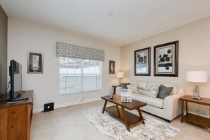 A living room with a sofa, coffee table, TV, and artwork on the walls. - Private Pool Townhome Storey Lake (Kissimmee)