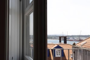 A view through a window with a balcony overlooking a harbor, buildings, and a distant hill. - Apartment 'Guerreiro - T2 2B' (Viana do Castelo)
