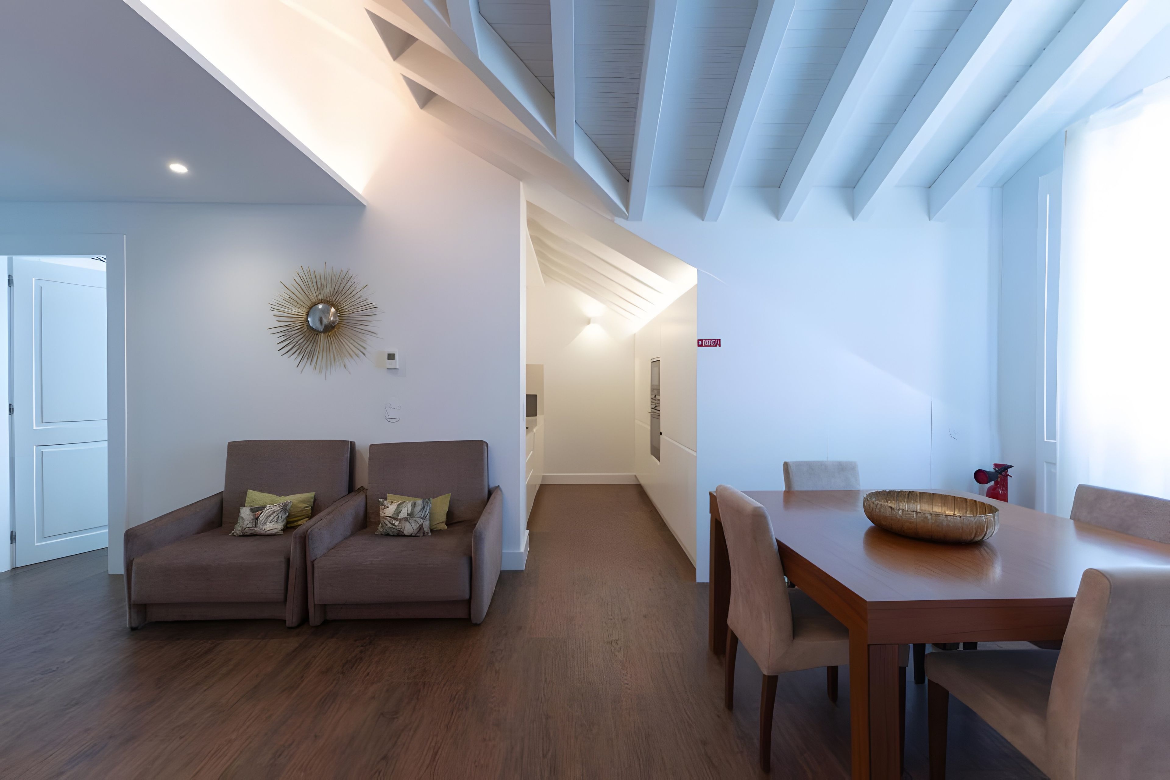 A modern living room with a sofa set, a dining table with chairs, and a decorative wall piece.