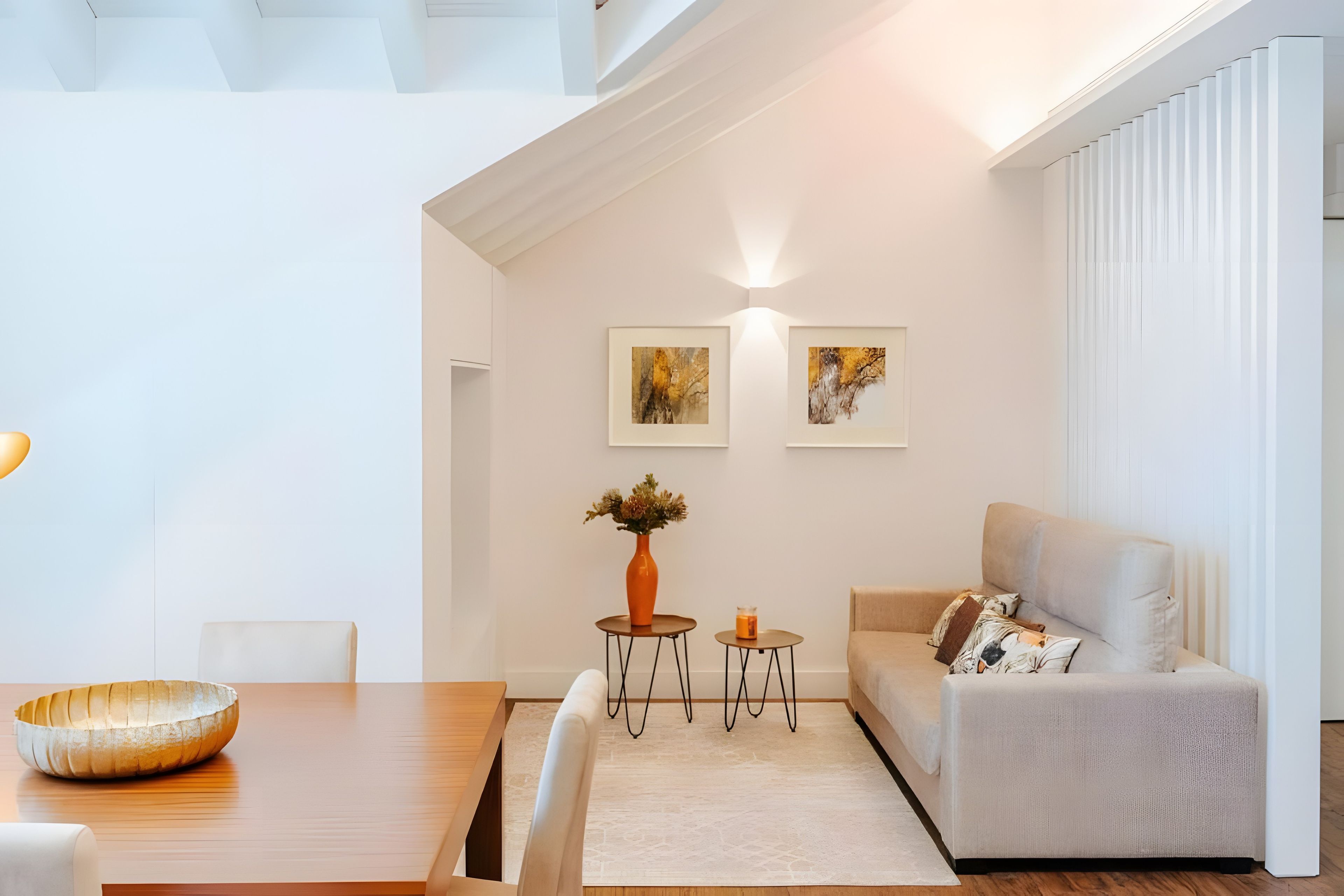 A modern living room with a dining area, featuring a sofa, a table, and two small side tables with decorative items.