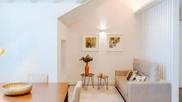 A modern living room with a dining area, featuring a sofa, a table, and two small side tables with decorative items.