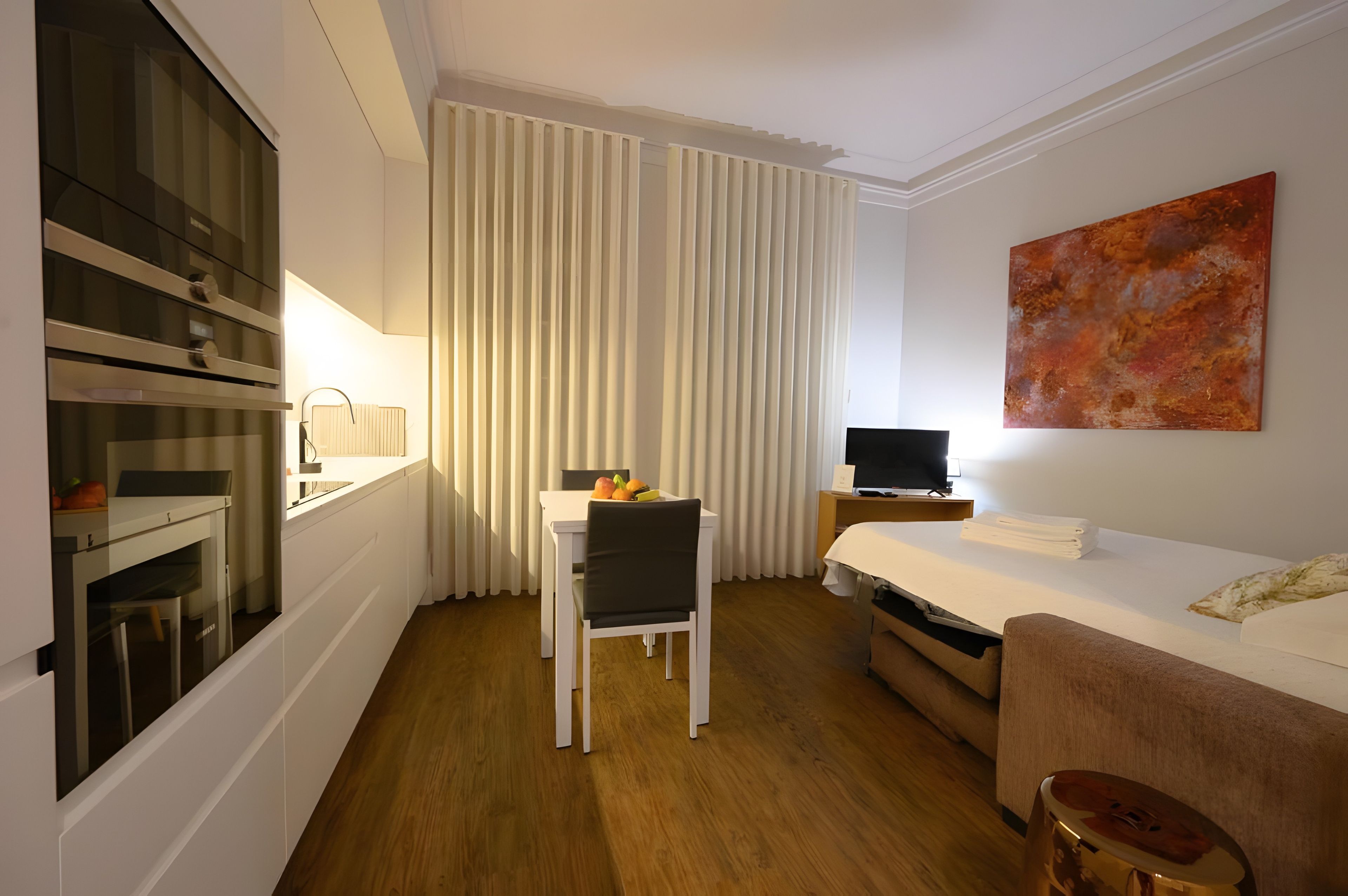 A hotel room with a bed, a desk with a chair, a television, and a large window with curtains.