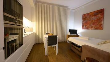 A hotel room with a bed, a desk with a chair, a television, and a large window with curtains.