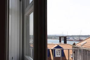 A view through a window with a balcony overlooking a harbor, buildings, and a distant hill. - Apartment 'Guerreiro - T2 3B' (Viana do Castelo)