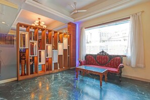 A room with a red sofa, a glass coffee table, a decorative wooden cabinet, and a large window with a view of buildings.