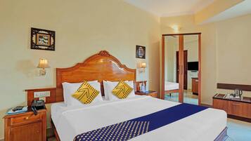 A hotel room with a large bed, wooden headboard, two bedside tables with lamps, a desk with a telephone, and a mirror.