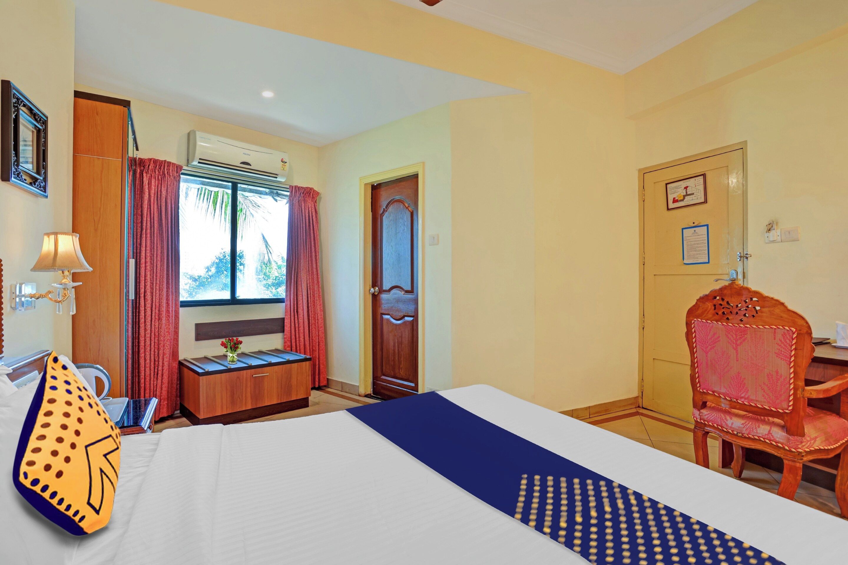Una habitación de hotel con cama, escritorio, silla, ventana con cortinas y aire acondicionado.