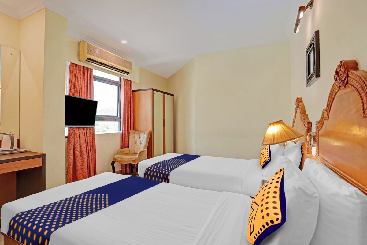 A hotel room with two beds, a desk, a chair, a television, and a window with curtains.